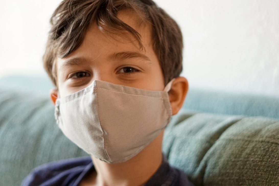 En ung pojke med ansiktsmask sitter inomhus, vilket illustrerar barns sårbarhet för inomhusluftens kvalitet.